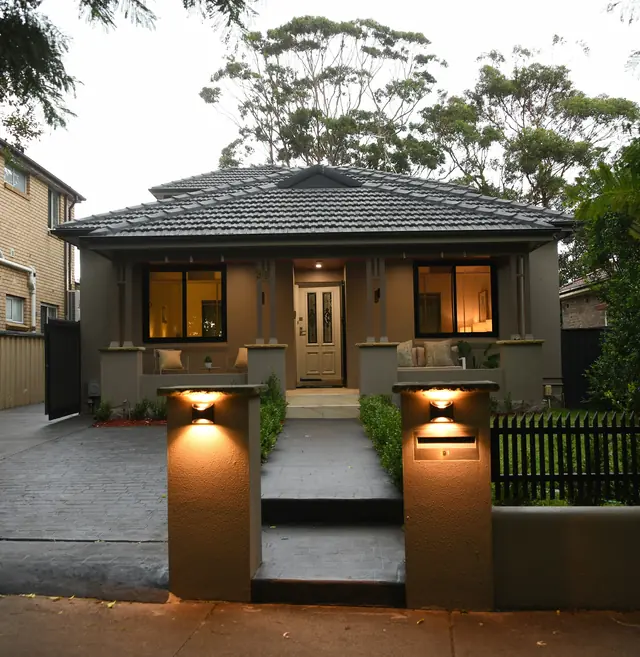 A house at dusk with wall lights glowing on its entrance pillars