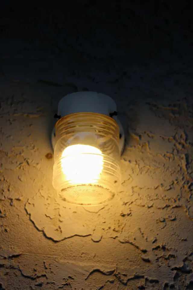 A wall-mounted porch light glowing warmly against a stucco wall