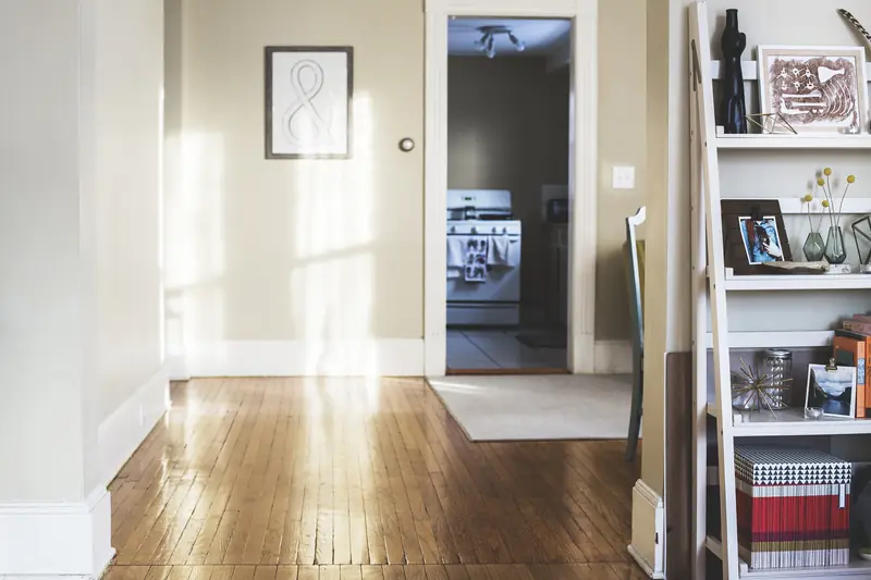 A sunlit hallway with polished wood floors and an open doorway