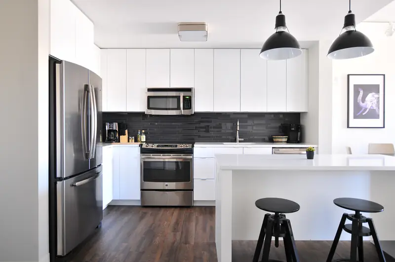 A clean white kitchen with stainless appliances and two black pendant lights