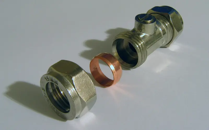 A brass shut-off valve, compression nut and copper olive laid out on a white surface