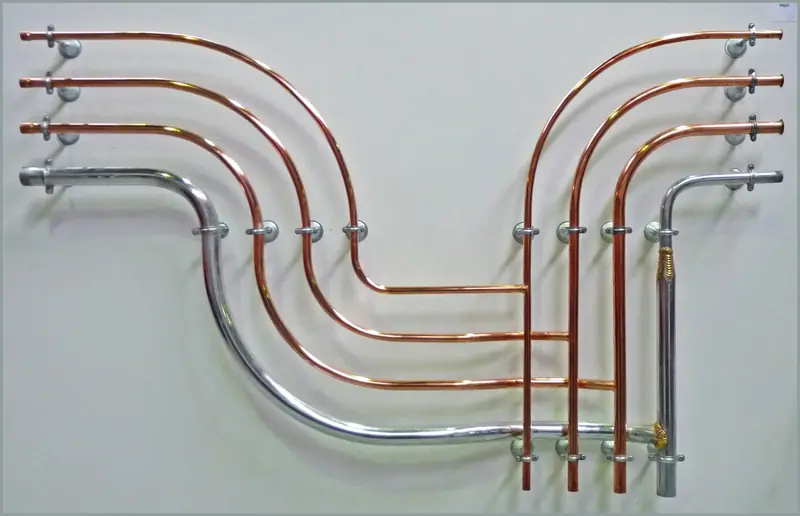 Copper and steel pipes bent in parallel curves and clipped to a pale wall