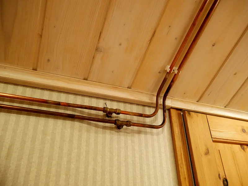 Copper water pipes running neatly along a wood-panelled ceiling