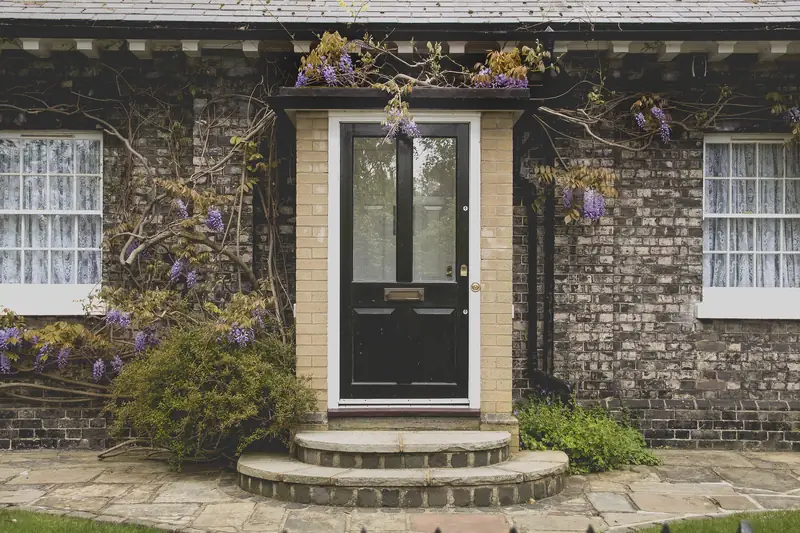 A black front door with stone steps, framed by wisteria on a brick house